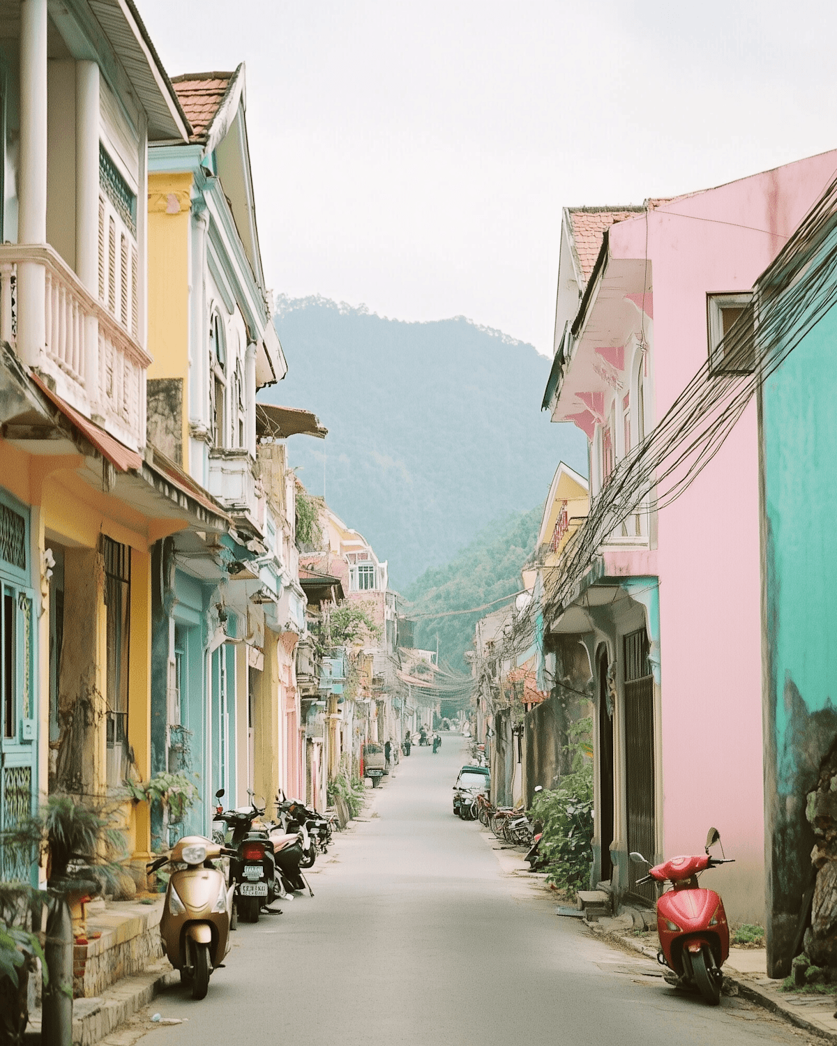 A pastel street of low buildings beneath green mountains